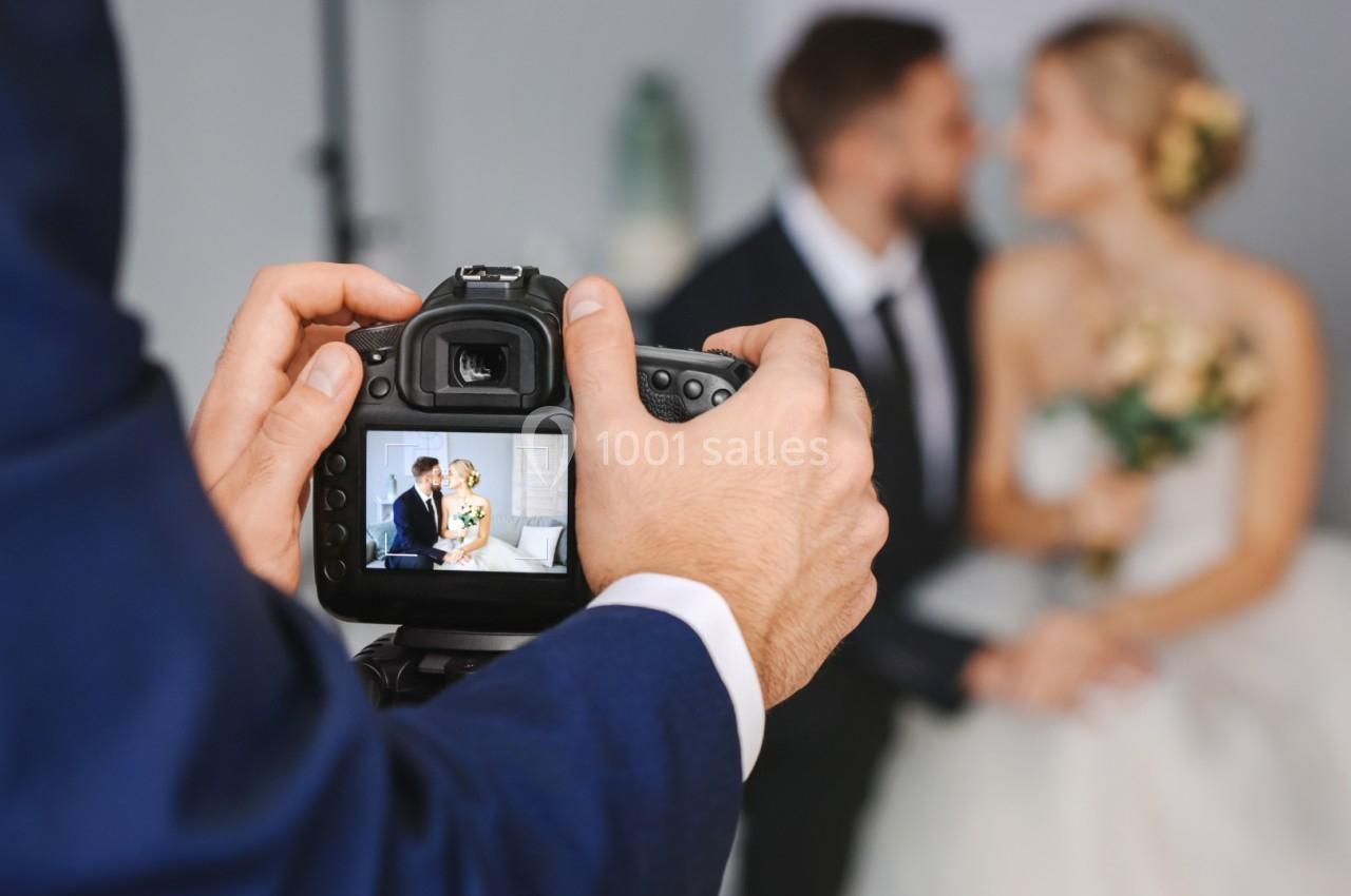 Un photographe capture un couple de mariés assis, visible à travers l'écran de l'appareil photo.