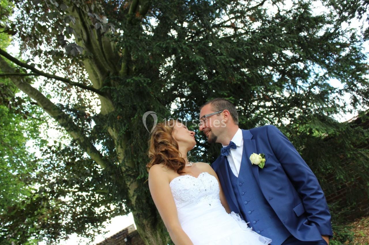 Un couple en tenue de mariage se regarde sous un grand arbre, dans un cadre extérieur verdoyant.