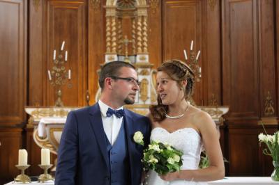 Un couple de mariés échange un regard complice devant l'autel d'une église ornée de bois sculpté.