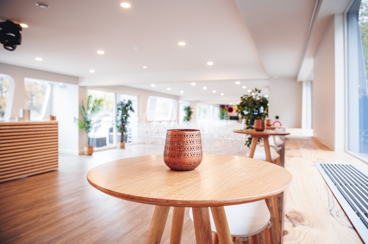 Salle lumineuse avec une table en bois au premier plan, décorée d'un photophore ajouré, et des plantes en arrière-plan.