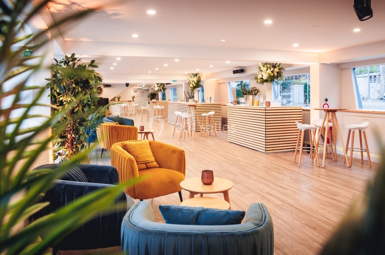 Espace lumineux avec fauteuils colorés, tables basses, comptoirs en bois et plantes décoratives.