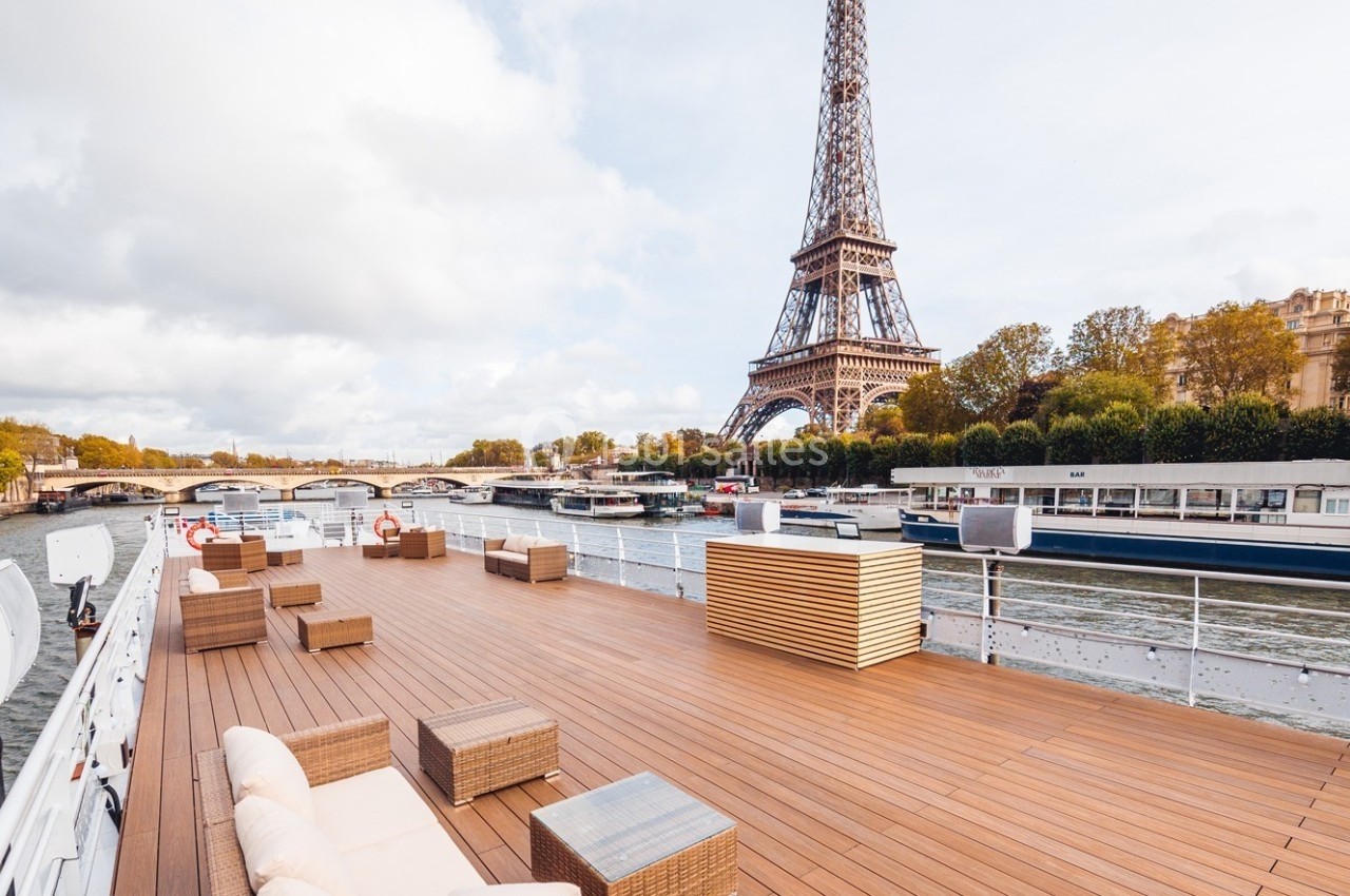 Pont en bois aménagé avec des sièges, offrant une vue sur la Seine et la tour Eiffel par temps partiellement nuageux.