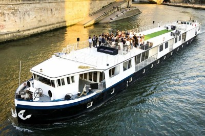 Bateau naviguant sur une rivière avec un groupe de personnes rassemblées sur le pont supérieur.