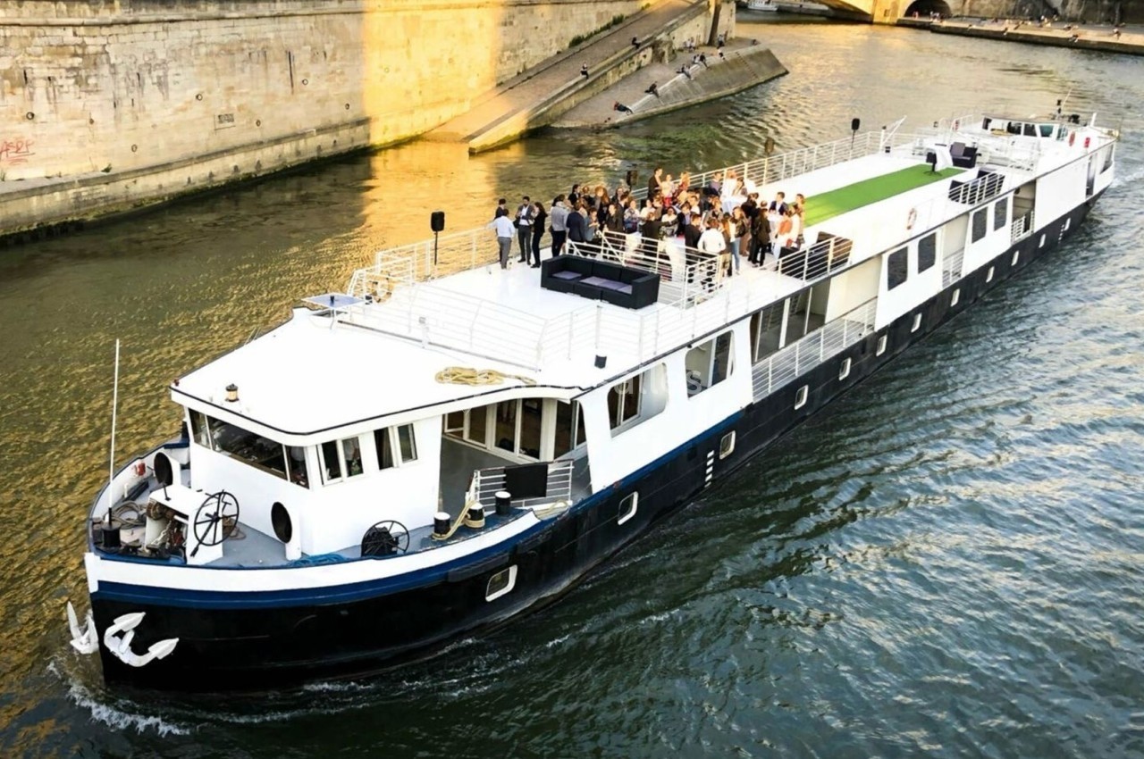 Bateau naviguant sur une rivière avec un groupe de personnes rassemblées sur le pont supérieur.