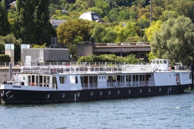 Bateau naviguant sur une rivière avec un groupe de personnes rassemblées sur le pont supérieur.