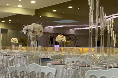 Salle de réception élégante avec tables dressées, décor floral blanc et rose, et chandeliers en verre.