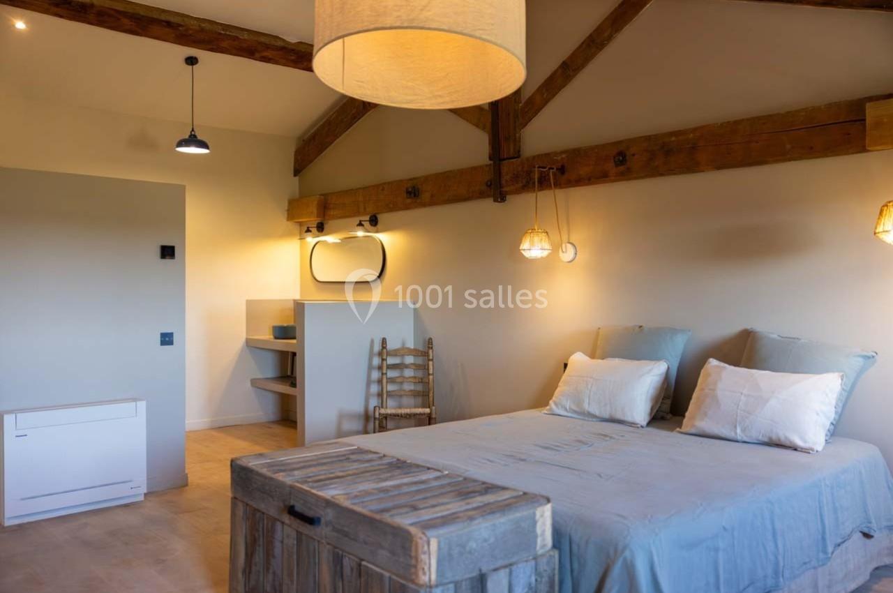 Chambre lumineuse avec poutres apparentes, lit double, éclairage suspendu et mobilier en bois rustique.