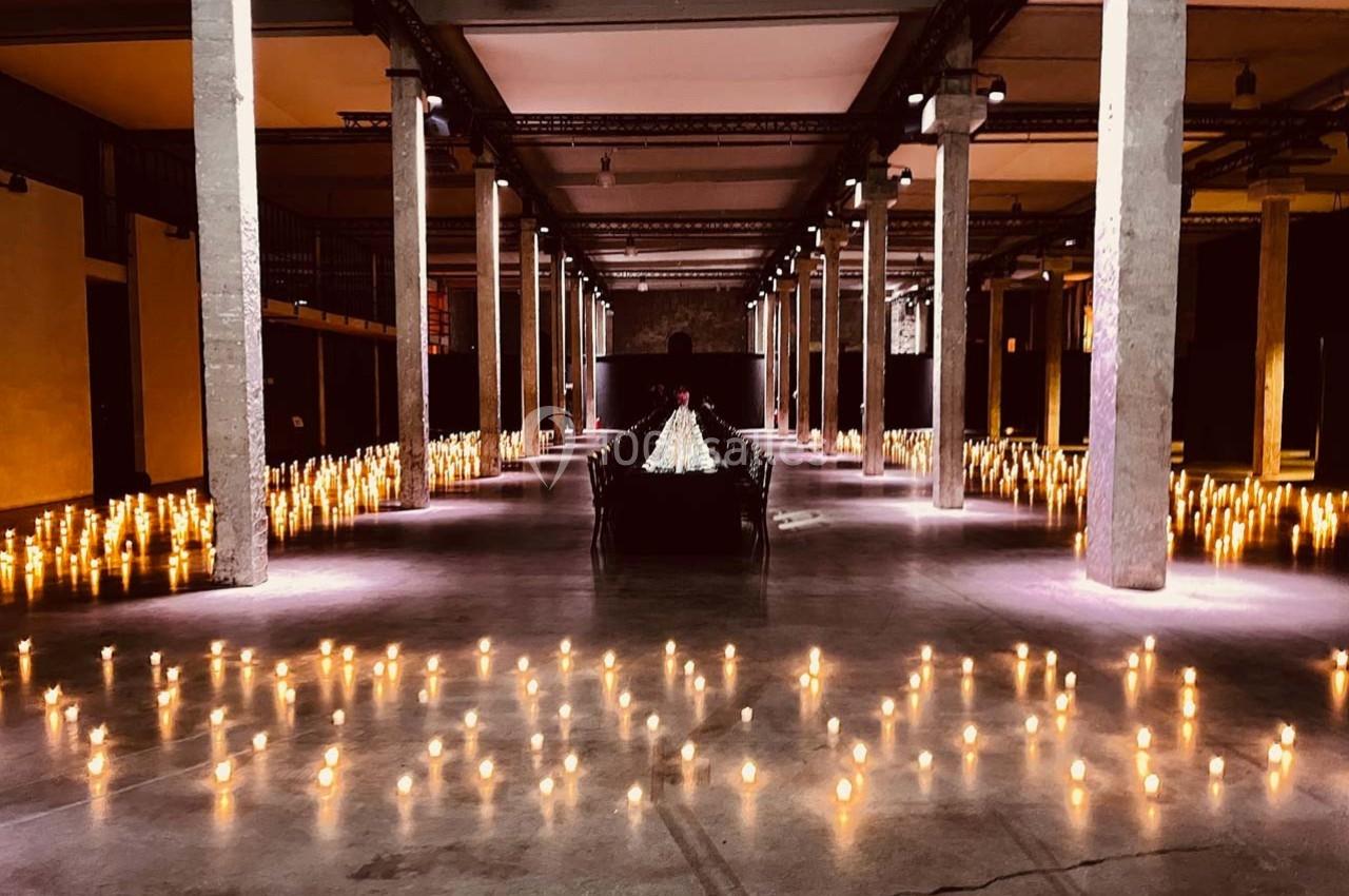 Salle industrielle éclairée par de nombreuses bougies disposées au sol, créant une ambiance chaleureuse et intime.
