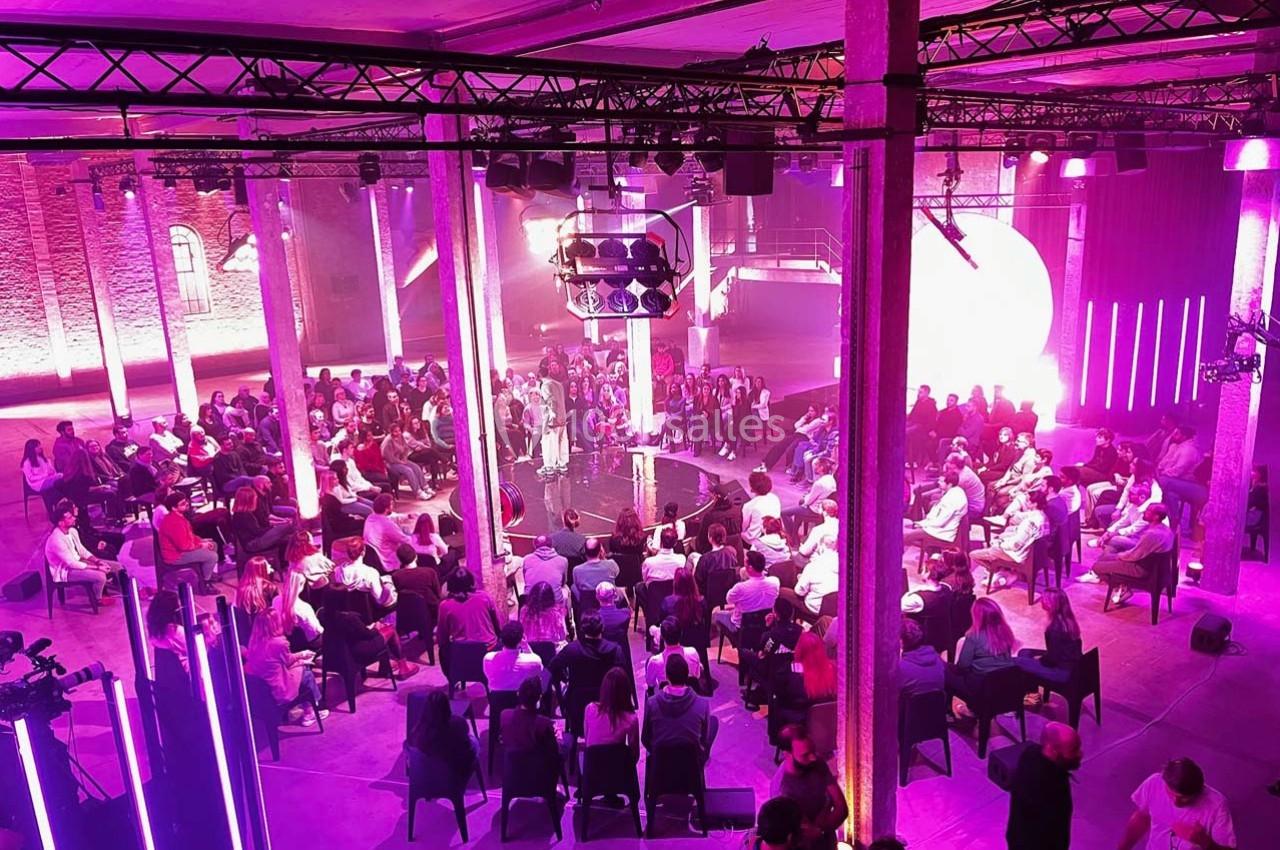 Vue d'une salle de conférence avec un public assis en cercle, éclairée par des lumières violettes et roses.