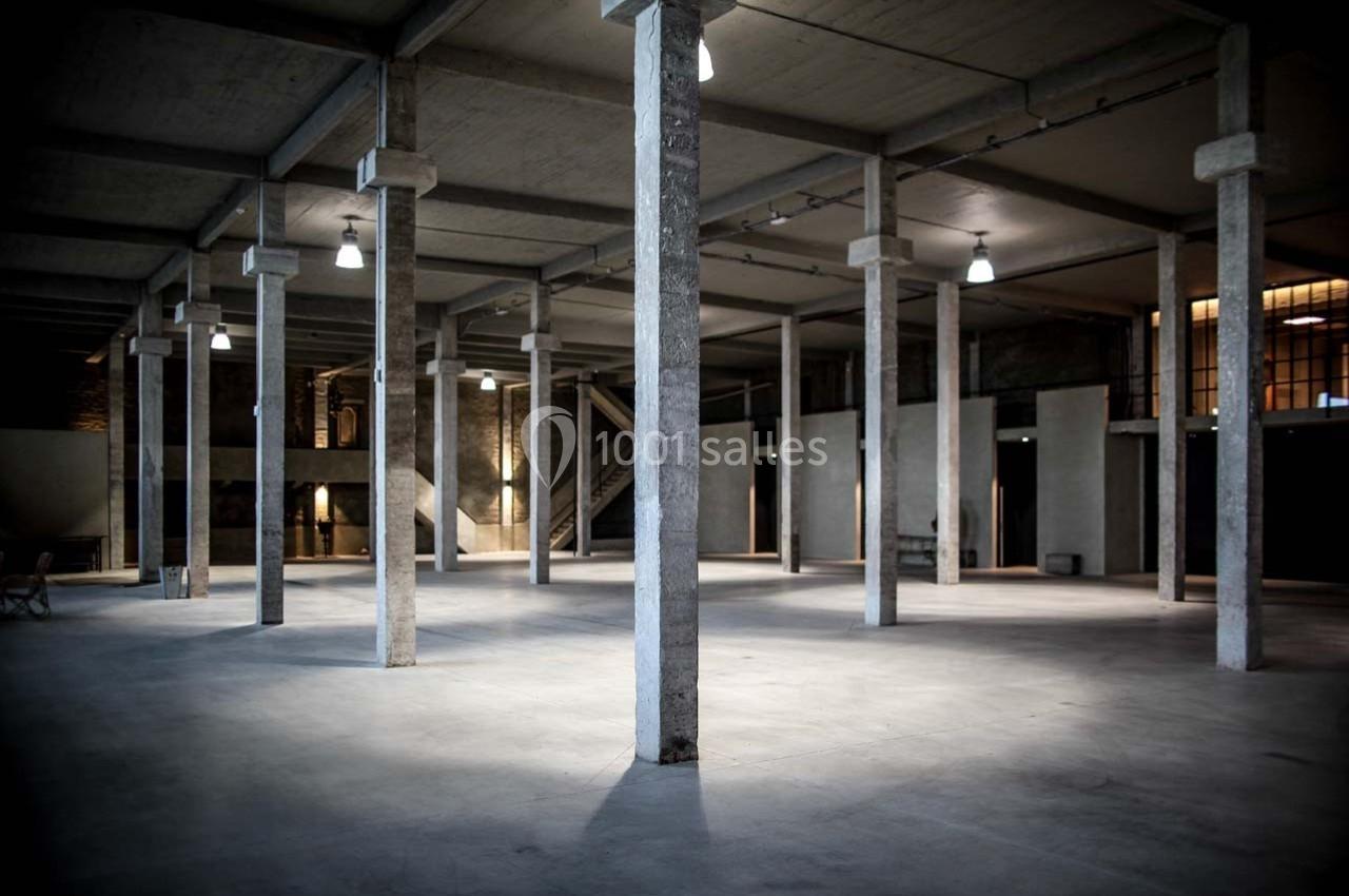 Intérieur d'un vaste entrepôt vide avec des colonnes en béton et un éclairage suspendu.