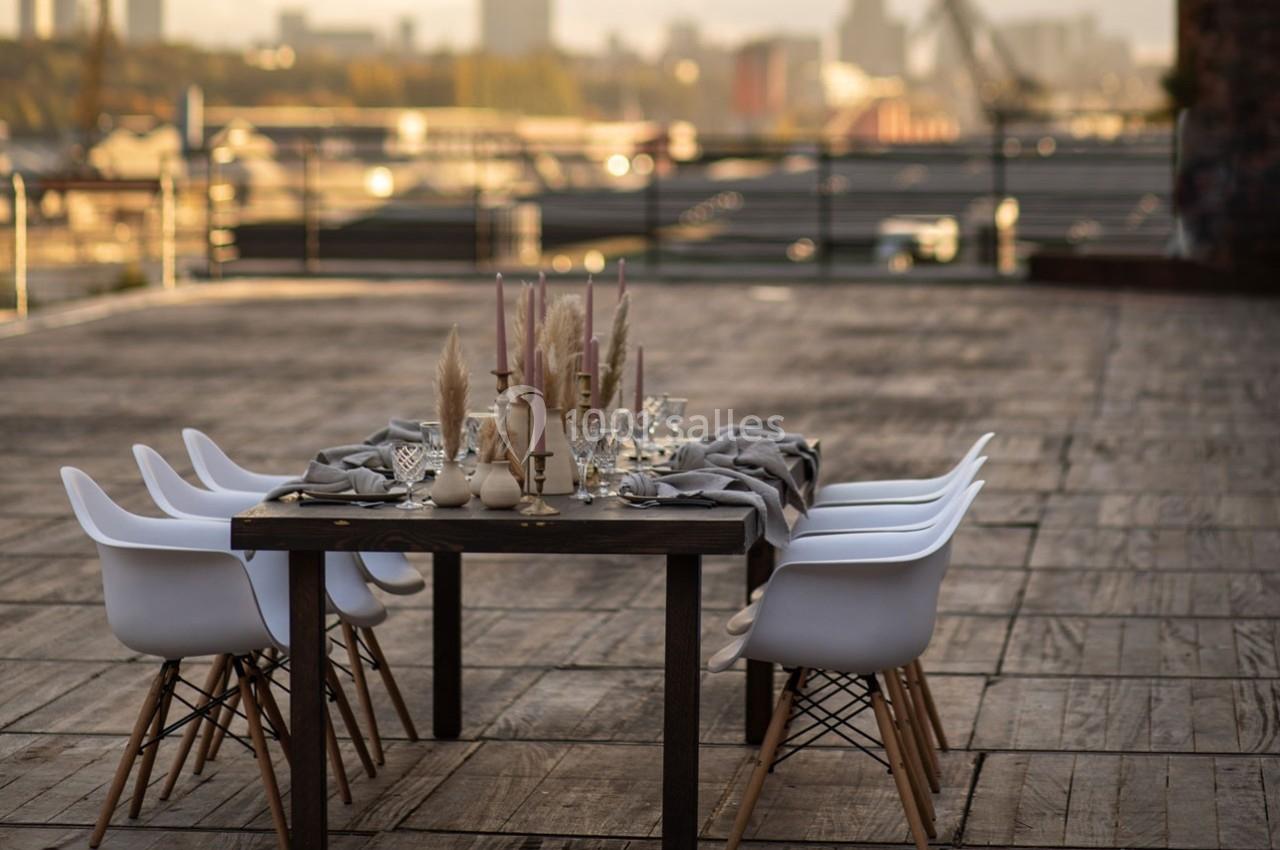 Table dressée avec des bougies et des décorations sur une terrasse en bois, vue sur une ville en arrière-plan.