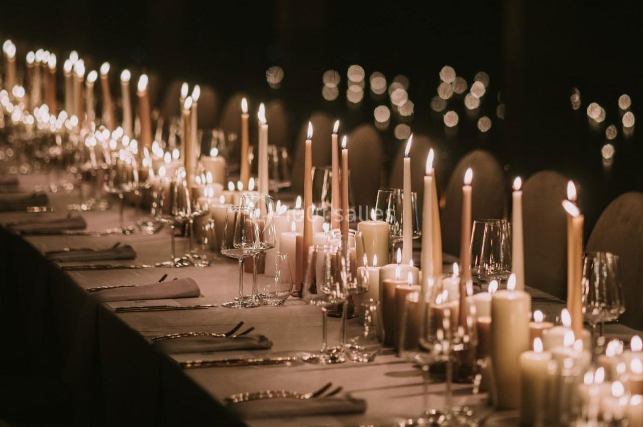 Table élégamment dressée avec des bougies allumées, verres et serviettes, créant une ambiance chaleureuse et intime.
