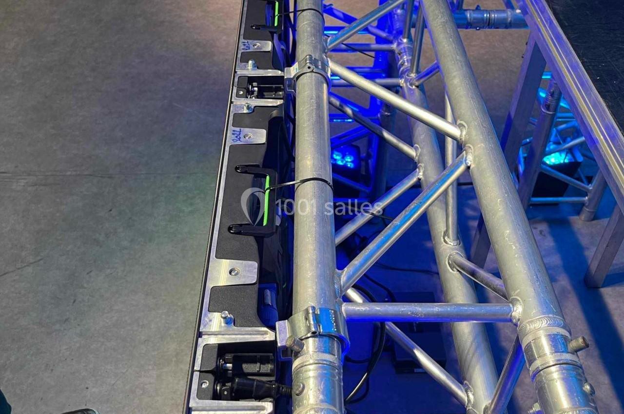 Structure métallique de scène avec des projecteurs alignés, posée sur un sol en béton dans un espace intérieur.