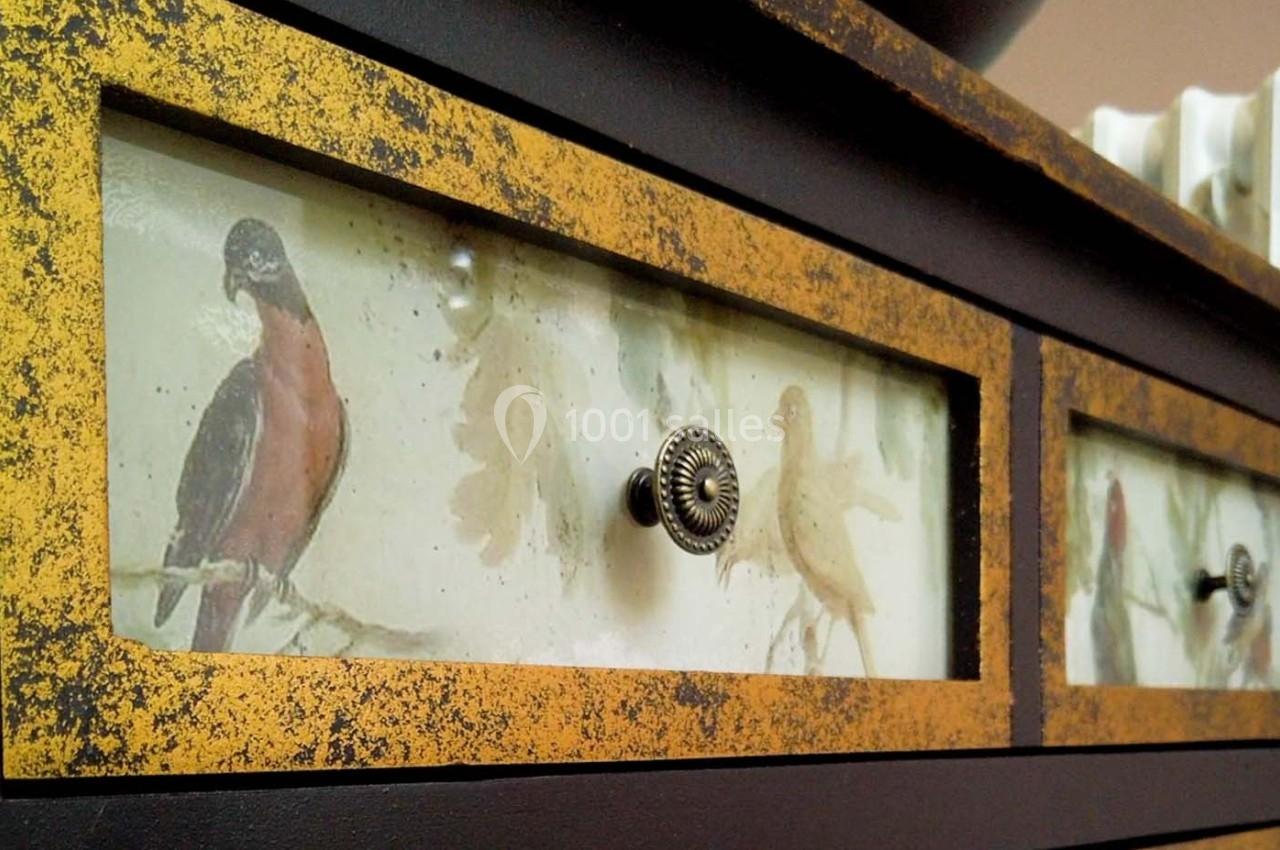 Tiroirs décorés de motifs d'oiseaux peints, encadrés de bois jaune vieilli avec poignées métalliques.