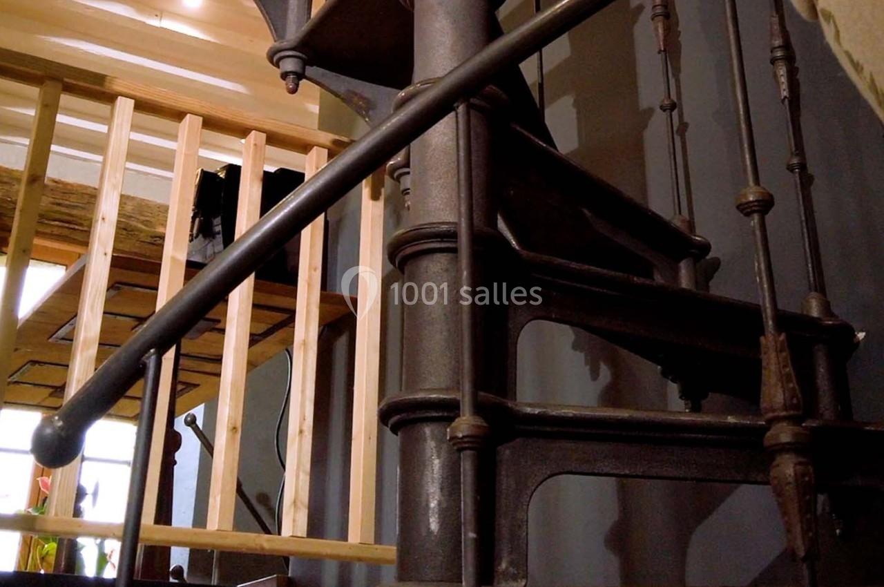 Escalier en colimaçon en métal noir avec des détails industriels, situé près d'une structure en bois.