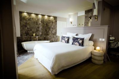 Chambre lumineuse avec lit double, fauteuil en bois, baignoire blanche et grande fenêtre donnant sur l'extérieur.