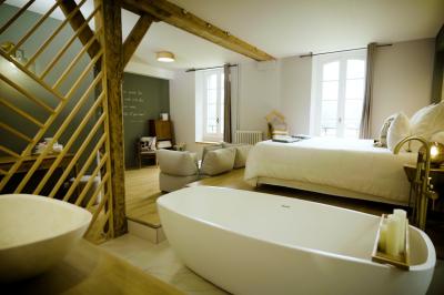 Chambre lumineuse avec lit double, fauteuil en bois, baignoire blanche et grande fenêtre donnant sur l'extérieur.