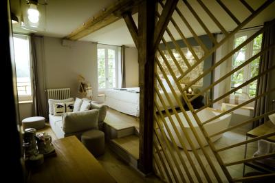 Chambre lumineuse avec lit double, fauteuil en bois, baignoire blanche et grande fenêtre donnant sur l'extérieur.