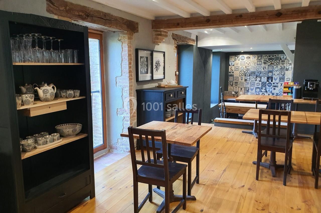 Salle à manger lumineuse avec tables en bois, chaises simples et étagères contenant vaisselle et verres.