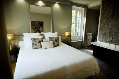 Chambre lumineuse avec lit double, fauteuil en bois, baignoire blanche et grande fenêtre donnant sur l'extérieur.