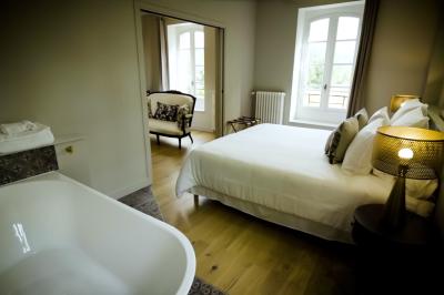 Chambre lumineuse avec lit double, fauteuil en bois, baignoire blanche et grande fenêtre donnant sur l'extérieur.