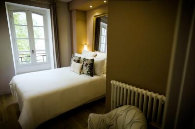 Chambre lumineuse avec lit double, fauteuil en bois, baignoire blanche et grande fenêtre donnant sur l'extérieur.