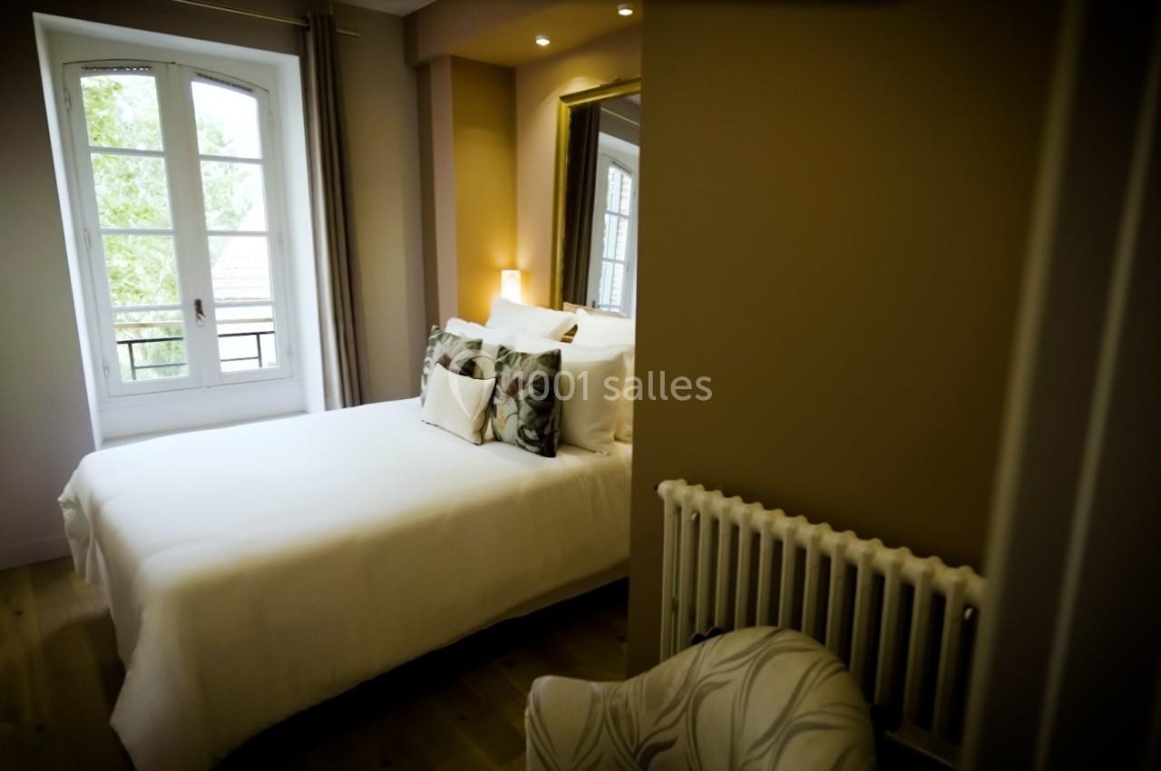 Chambre lumineuse avec lit double, oreillers décoratifs, grande fenêtre et radiateur sous un miroir mural.