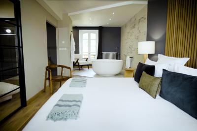 Chambre lumineuse avec lit double, fauteuil en bois, baignoire blanche et grande fenêtre donnant sur l'extérieur.