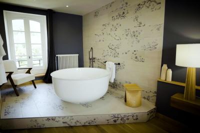 Chambre lumineuse avec lit double, fauteuil en bois, baignoire blanche et grande fenêtre donnant sur l'extérieur.