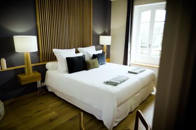 Chambre lumineuse avec lit double, fauteuil en bois, baignoire blanche et grande fenêtre donnant sur l'extérieur.