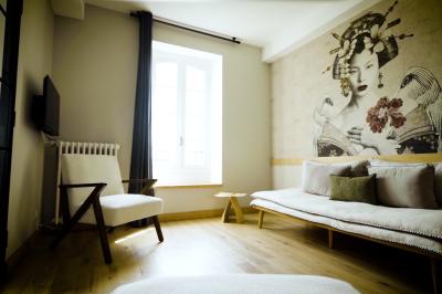 Chambre lumineuse avec lit double, fauteuil en bois, baignoire blanche et grande fenêtre donnant sur l'extérieur.
