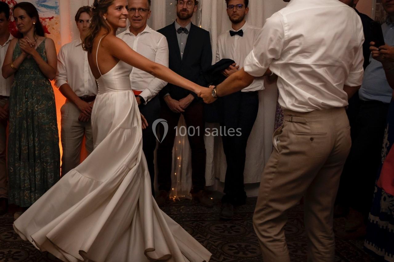 Un couple danse lors d'une réception, entouré d'invités debout dans une salle éclairée de lumières tamisées.