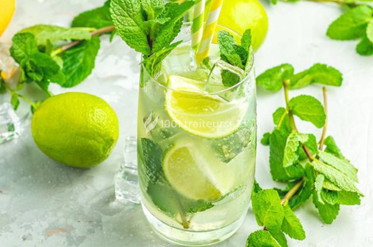 Verre de mojito garni de feuilles de menthe, rondelles de citron vert et glaçons, posé sur une surface claire.