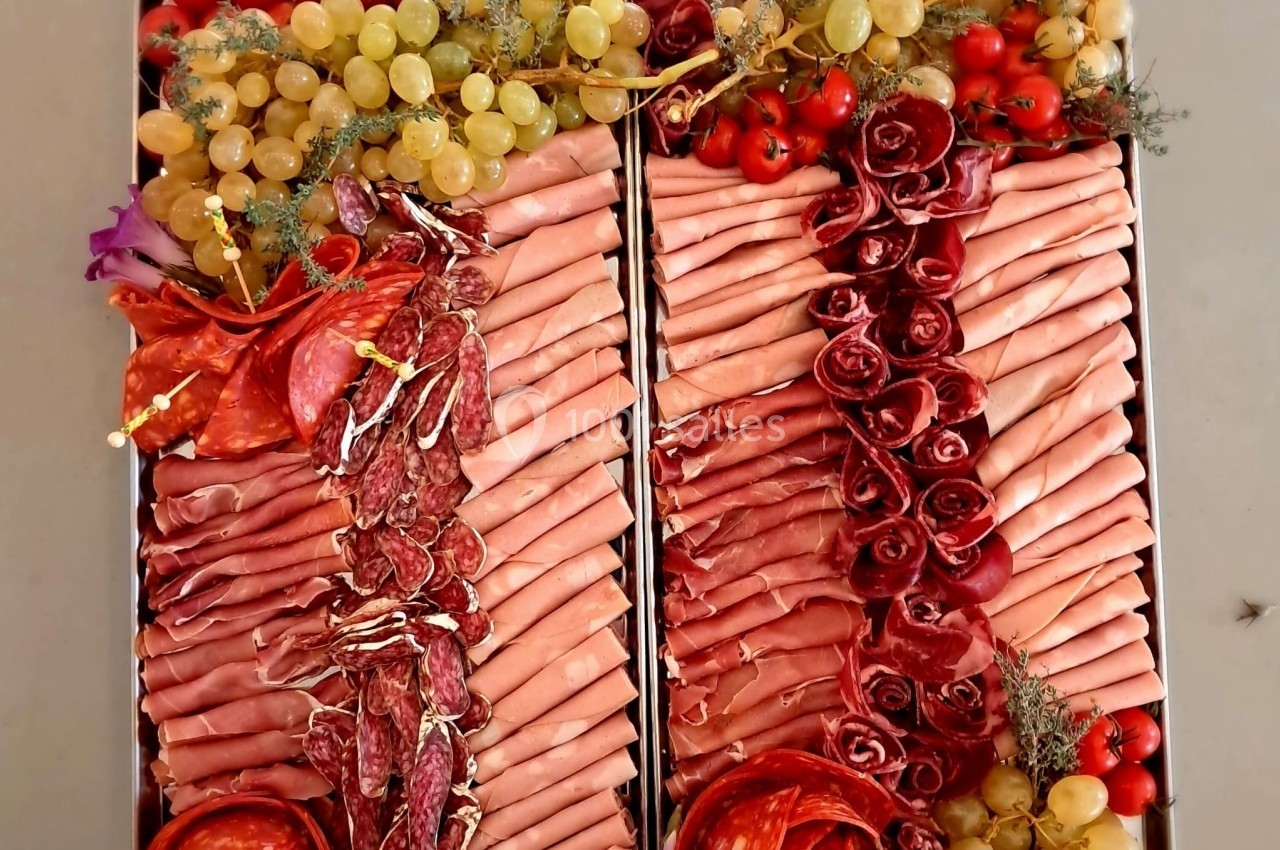 Plateau de charcuterie décoré avec des tranches de viande, raisins, tomates cerises et fleurs comestibles.