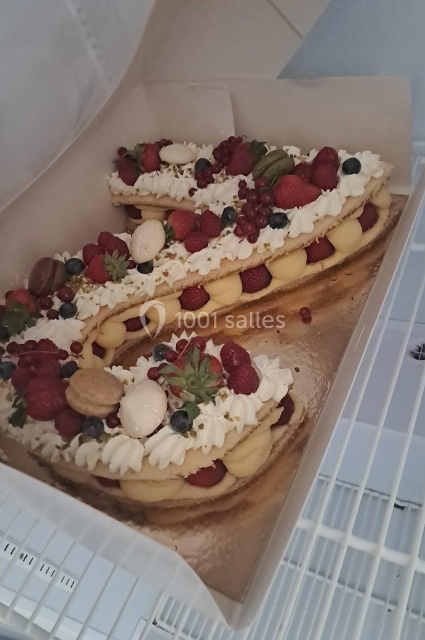 Gâteau en forme de chiffre décoré de crème, fruits rouges, macarons et meringues, présenté dans une boîte ouverte.