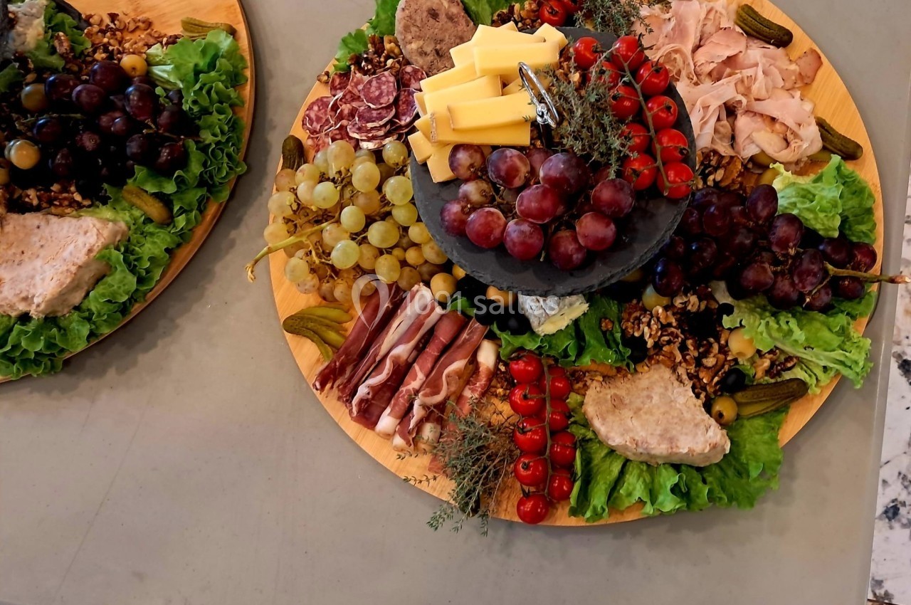 Plateau de charcuterie et fromages avec raisins, tomates cerises, cornichons, noix et feuilles de salade.