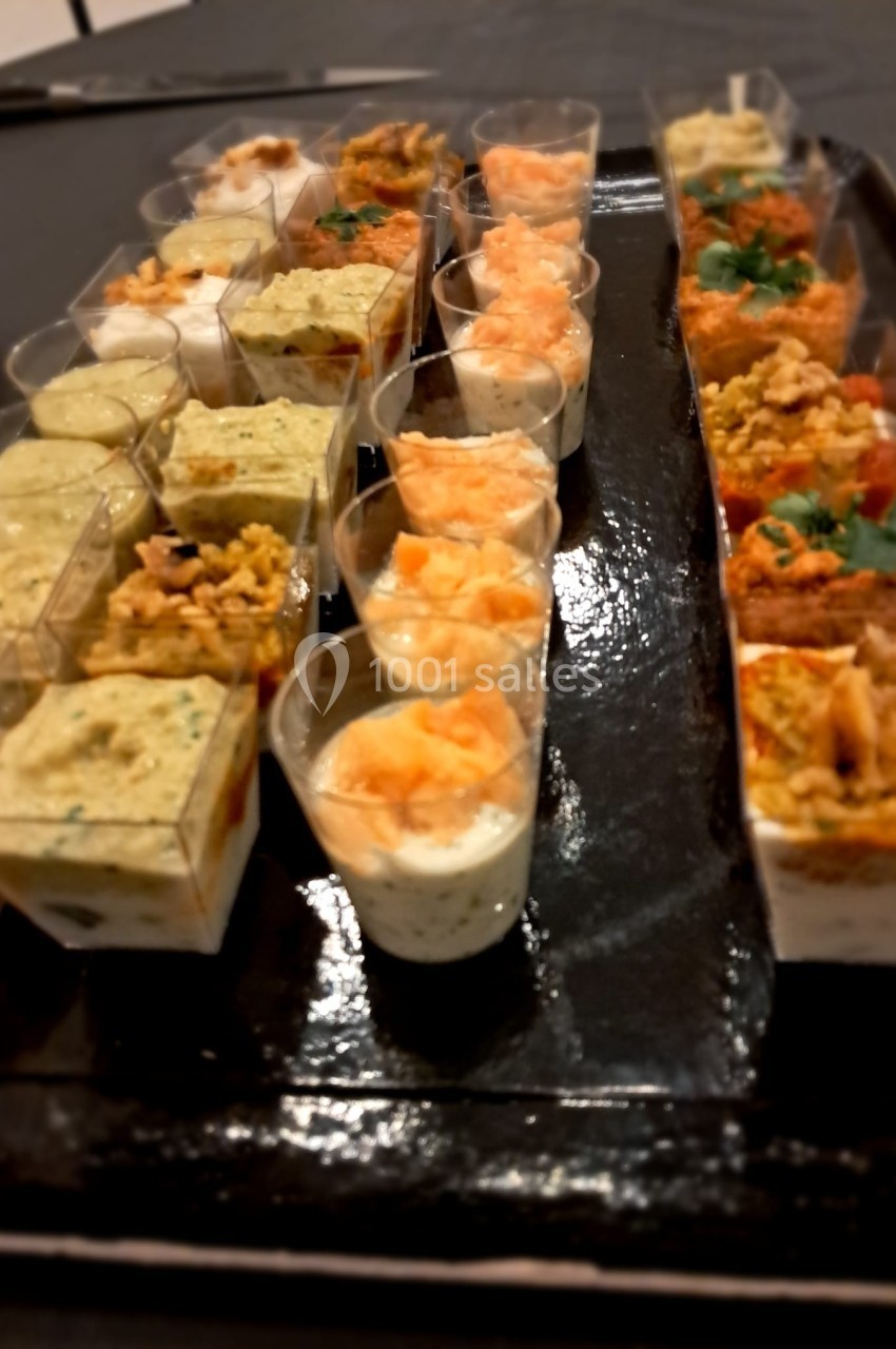 Plateau de verrines et bouchées salées variées disposées en rangées sur une table noire.