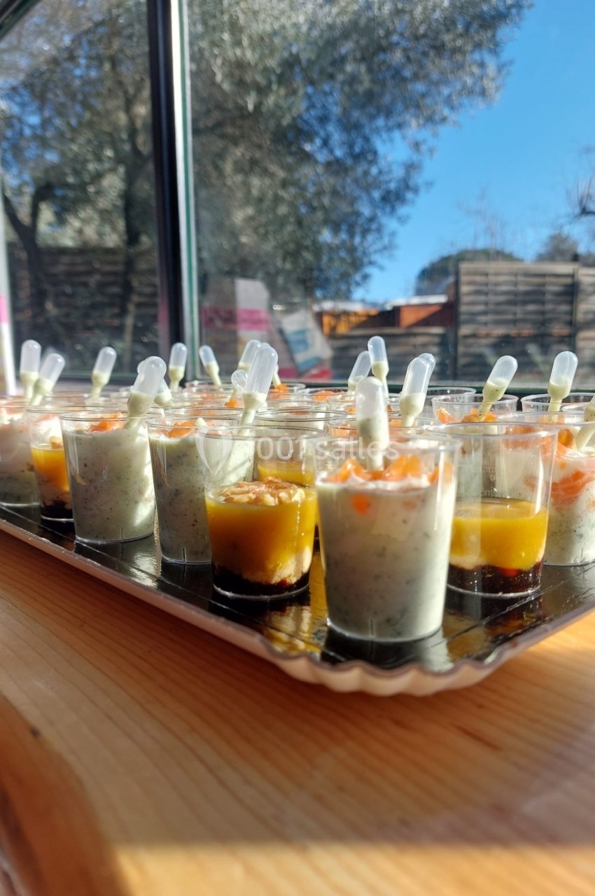 Plateau de verrines variées avec des pipettes, disposé sur une table en bois près d'une fenêtre ensoleillée.