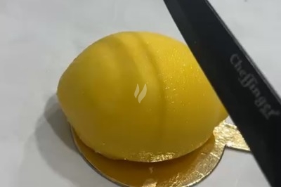 Un couteau s'apprête à couper un dessert en forme de citron posé sur un support doré.