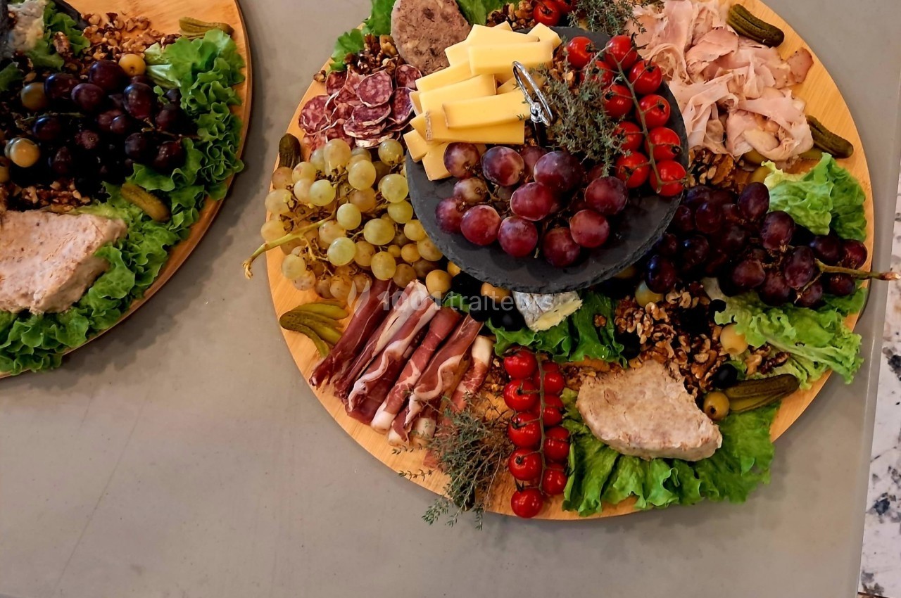 Plateau de charcuterie et fromages avec raisins, tomates cerises, cornichons, noix et feuilles de salade.