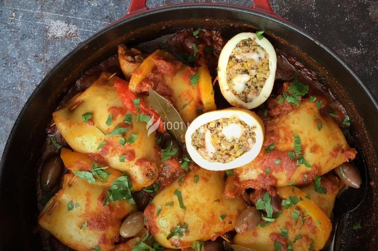 Calamars farcis cuits dans une sauce tomate avec des olives, des herbes fraîches et des épices, présentés dans une cocotte.