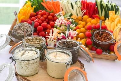 Plat de tajine en terre cuite contenant un mélange de légumes, olives et viande, avec théière et couscous en arrière-plan.