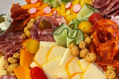 Plat de tajine en terre cuite contenant un mélange de légumes, olives et viande, avec théière et couscous en arrière-plan.