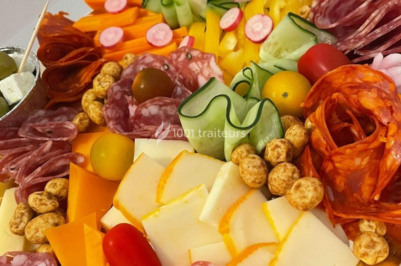 Plateau coloré de charcuteries, fromages, légumes frais, tomates cerises et olives, présenté pour un apéritif.
