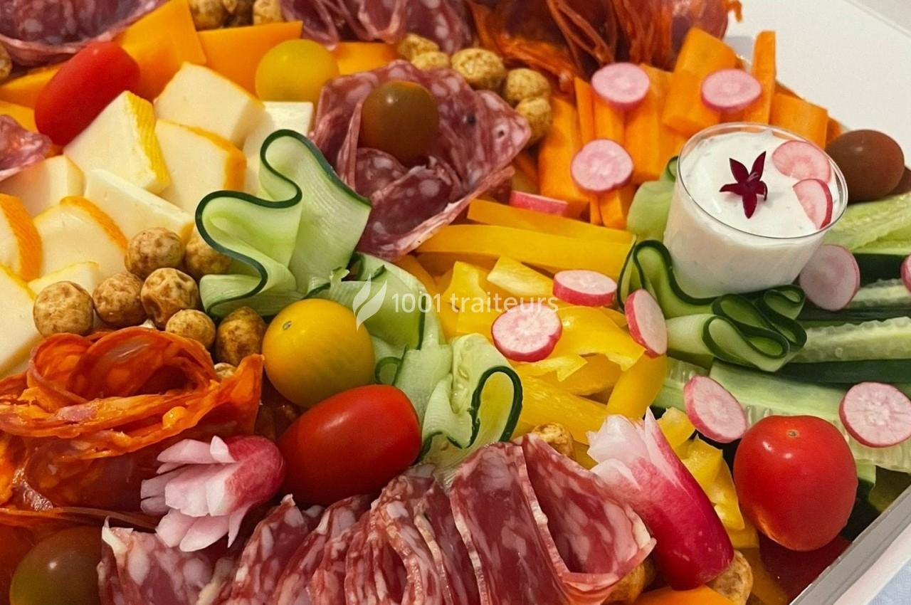 Plateau coloré composé de charcuteries, légumes frais, fromages, tomates cerises et une sauce blanche en accompagnement.