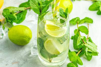 Plat de tajine en terre cuite contenant un mélange de légumes, olives et viande, avec théière et couscous en arrière-plan.