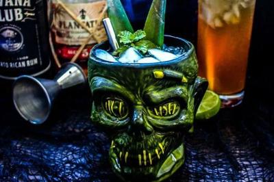 Plat de tajine en terre cuite contenant un mélange de légumes, olives et viande, avec théière et couscous en arrière-plan.