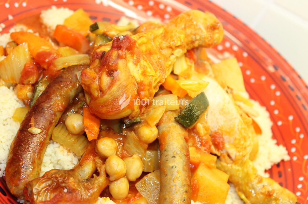 Plat de couscous avec légumes, pois chiches, merguez et pilon de poulet, servi sur une assiette rouge.