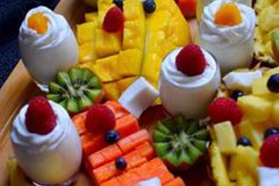 Plat de tajine en terre cuite contenant un mélange de légumes, olives et viande, avec théière et couscous en arrière-plan.