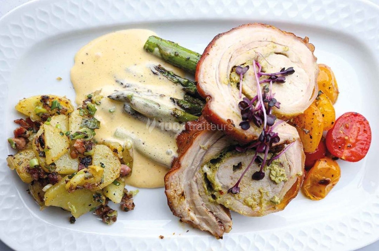 Assiette composée de rôti farci, asperges nappées de sauce, pommes de terre sautées et légumes rôtis.